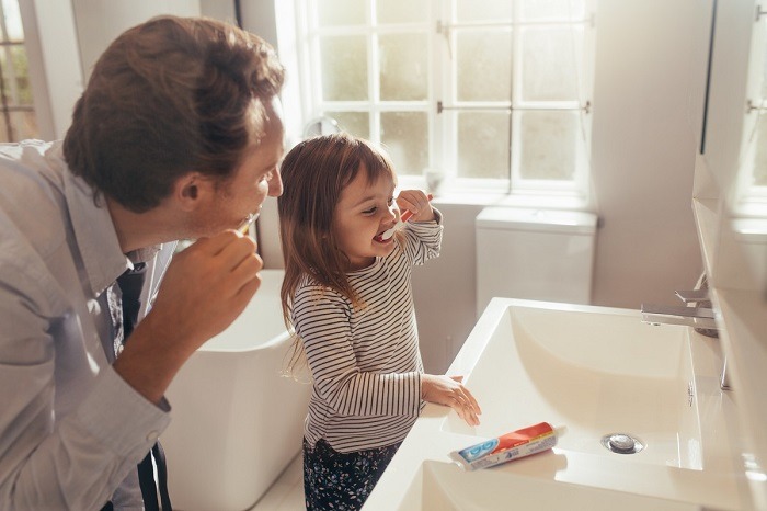 Father and daughter brushing teeth standing in bathroom.