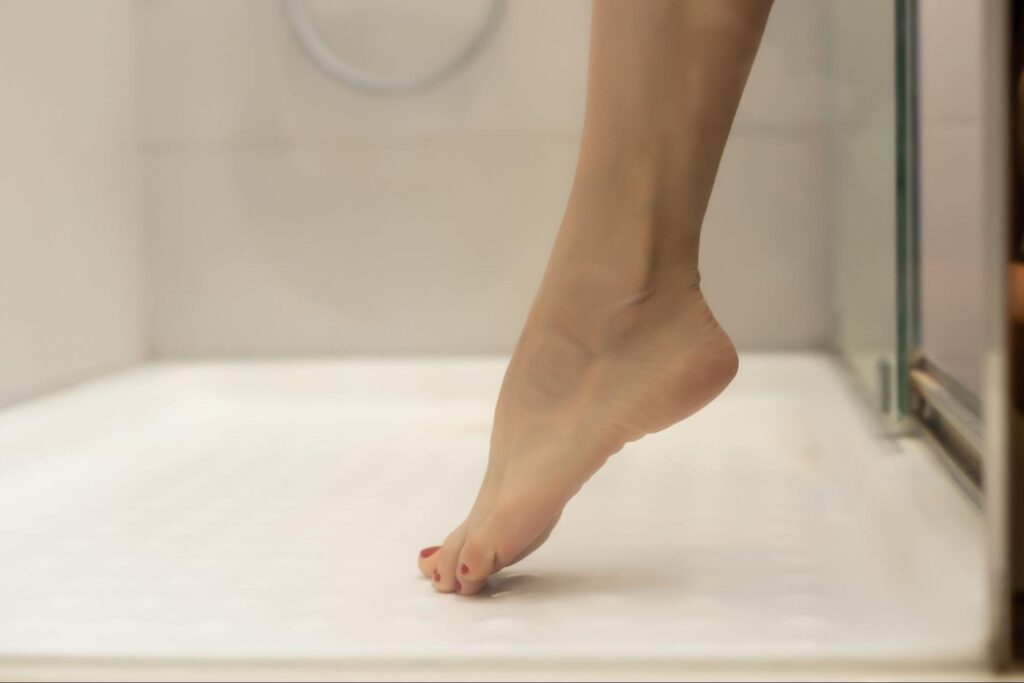 Woman taking a shower and standing on the shower pan.