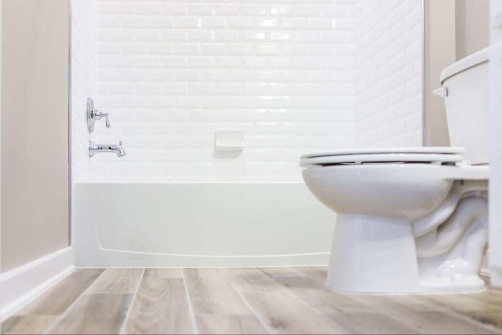 Modern white plain clean toilet bathroom with shower tiles and hardwood floors from ground level.