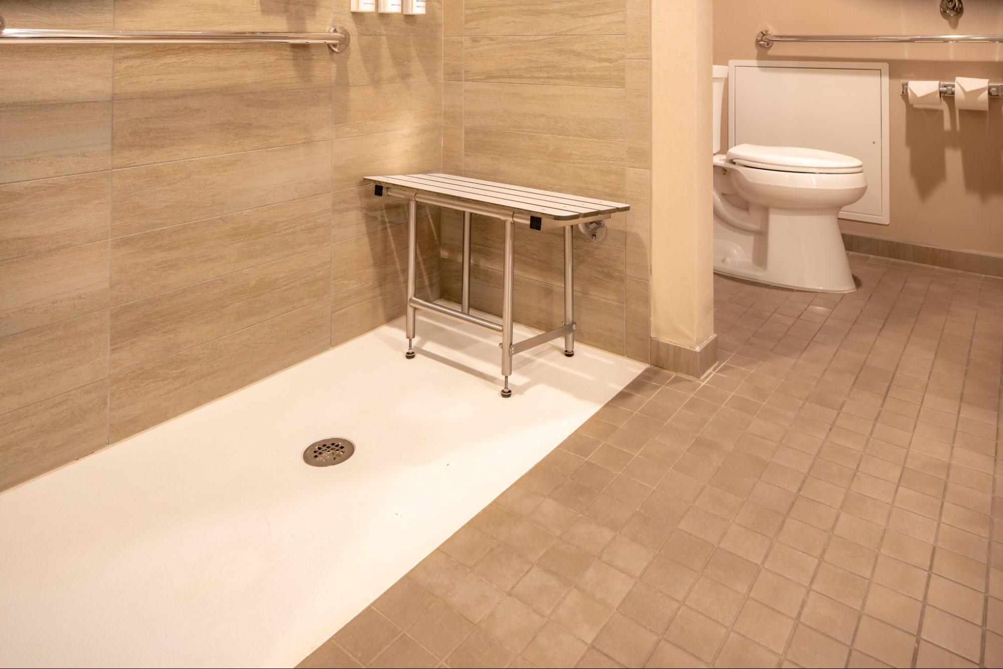 Wheelchair accessible hotel bathroom shower with tile floor and walls.